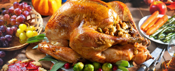 Roasted turkey on holiday table with pumpkins, pie, fruits, flowers and wine.