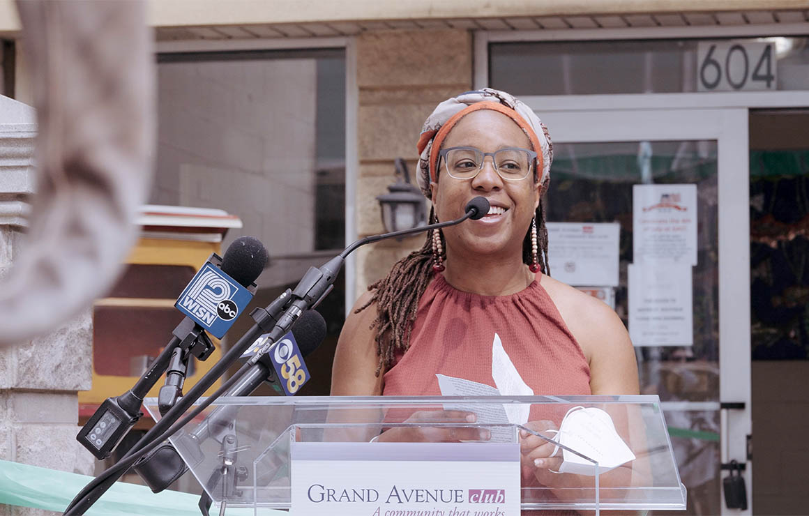 Artist Tia Richardson speaks at a podium in front of the Grand Avenue Mural.