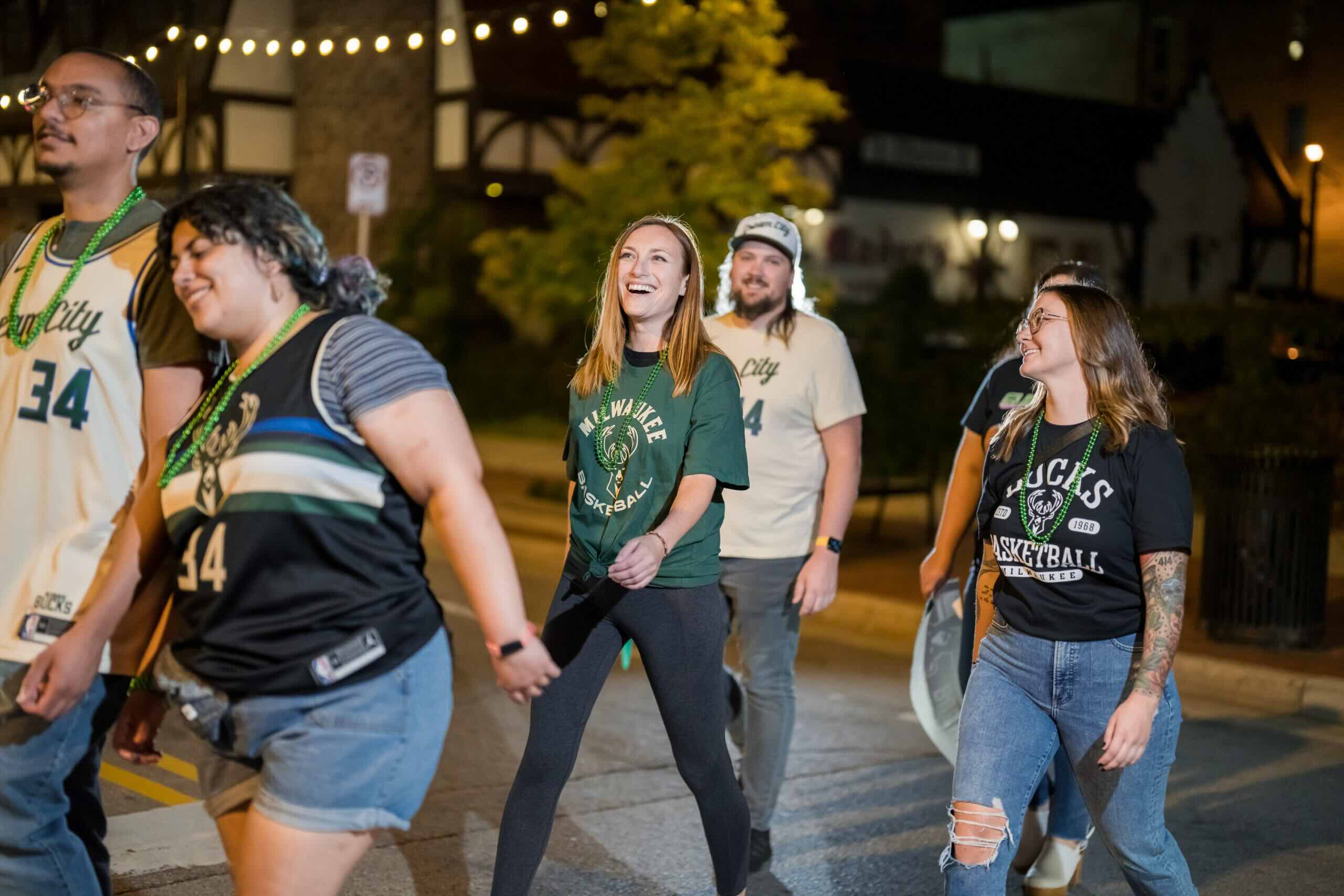 Group of people at night smiling and wearing Milwaukee Bucks apparel.