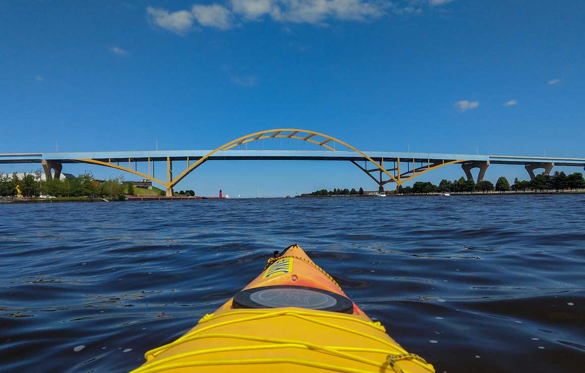 The front of a kayak on the river near the Hoan bridge.