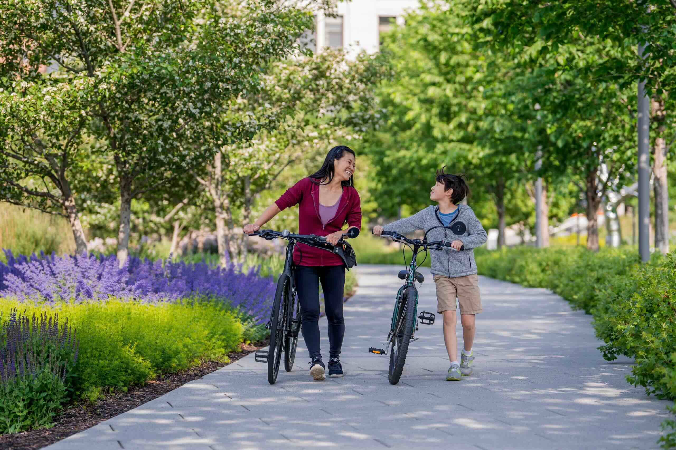 img_MDI_BrandingSenses2023_crFrontRoom_062-scaled (1) A mother and her son walk their bicycles along a path.