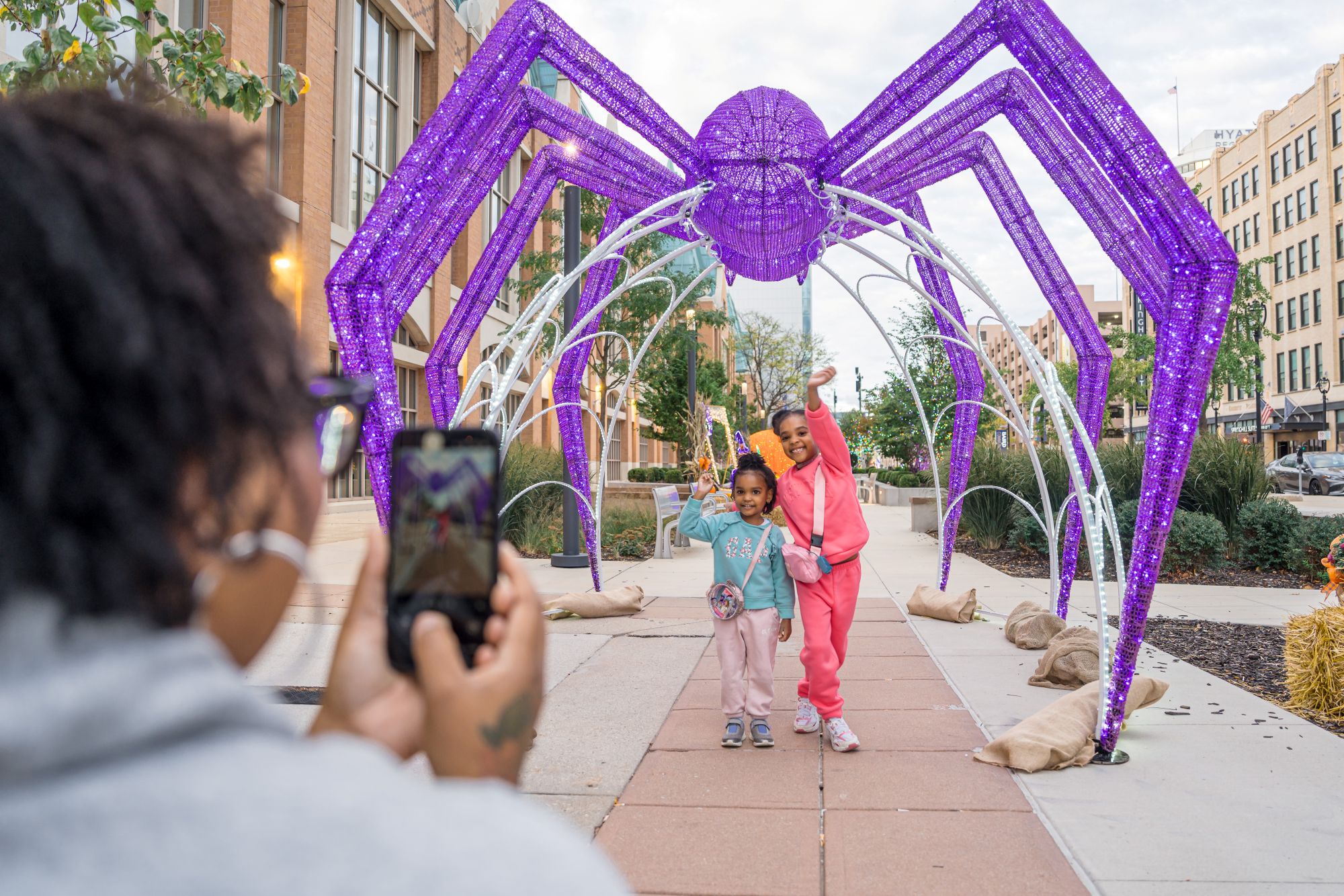 HalloweenVillage_FRPhoto_251015N_C1_022 girls posing under giant spider at Halloween Village
